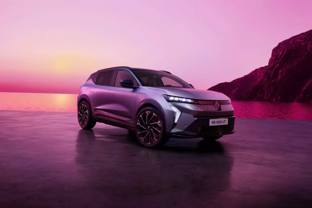 Renault Scénic E‑Tech vu de l’extérieur, finition argent, sous un ciel rose au coucher du soleil. face avant sculptée innovante